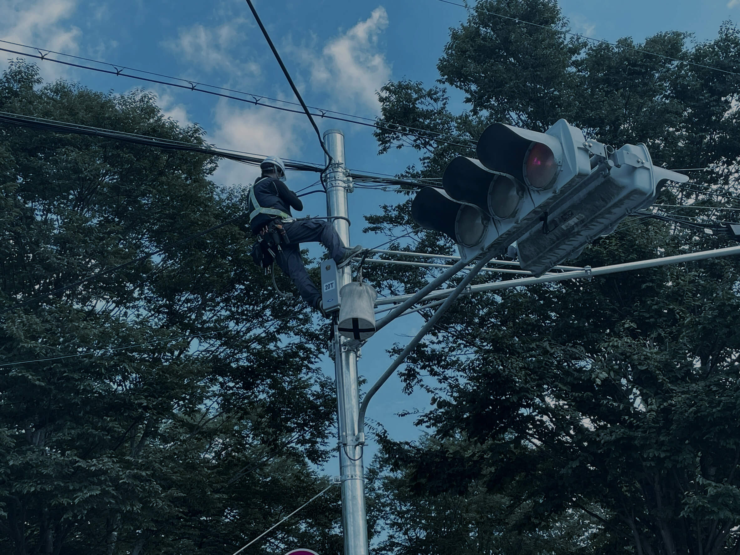 信号機のかなり高い位置まで登って配線作業を行う作業員。